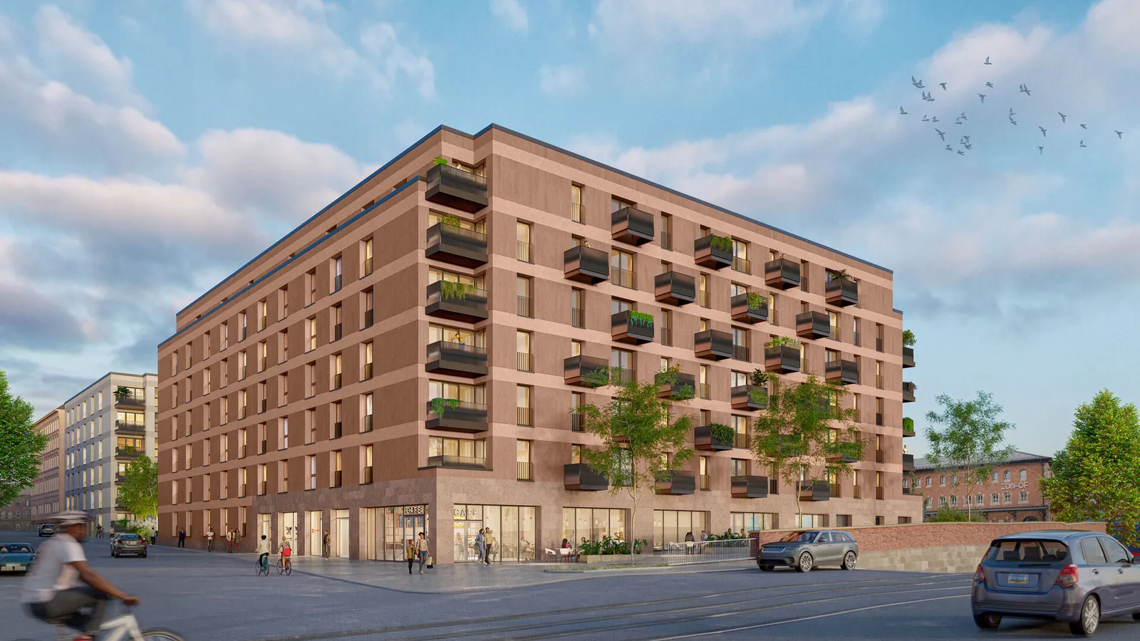 Strassenecke der Stromerhoefe: terrakottafarbene Putzfassade mit bodentiefen Fenstern, davor Baeume und Gehweg
